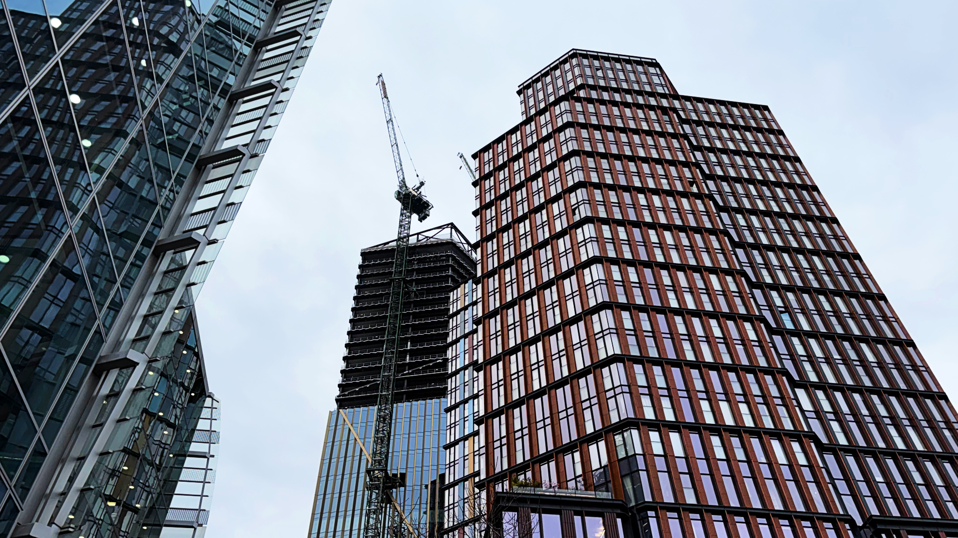 A construction crane and buildings viewed from street level in London.